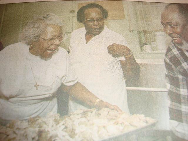 A woman holds a pan of food while two other people watch